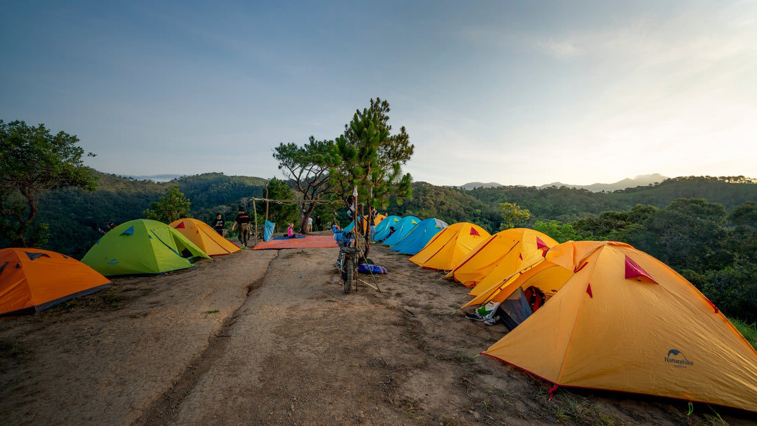 Colorful tents set up on a dirt road with a scenic background of trees and mountains.