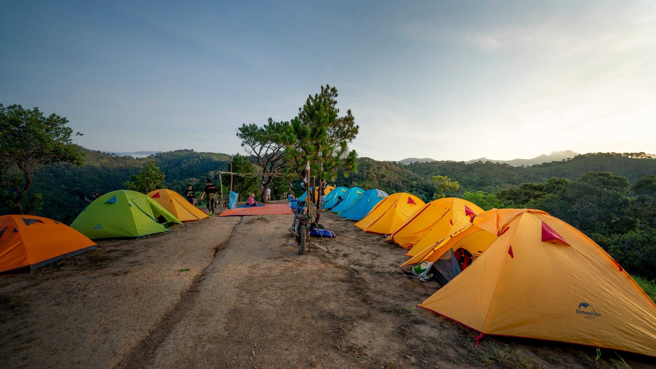 Colorful tents set up on a dirt road with a scenic background of trees and mountains.