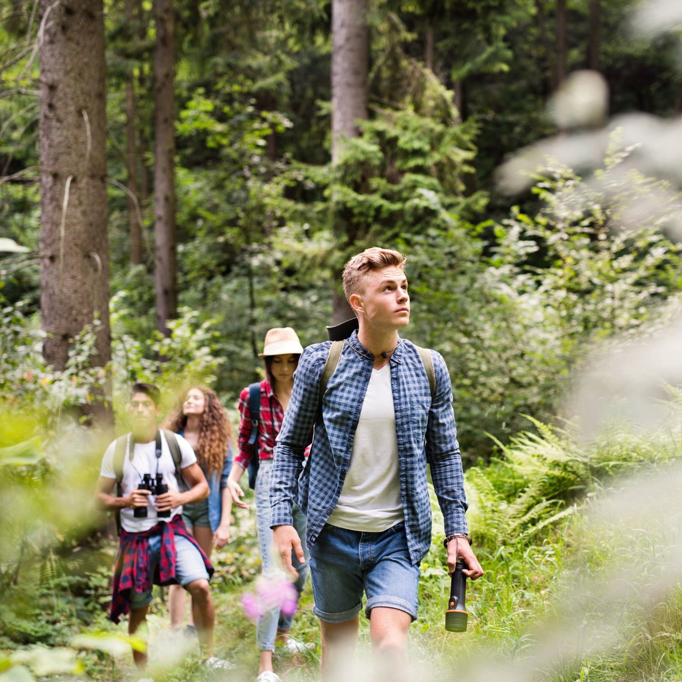Young man leading group of hikers through lush green forest